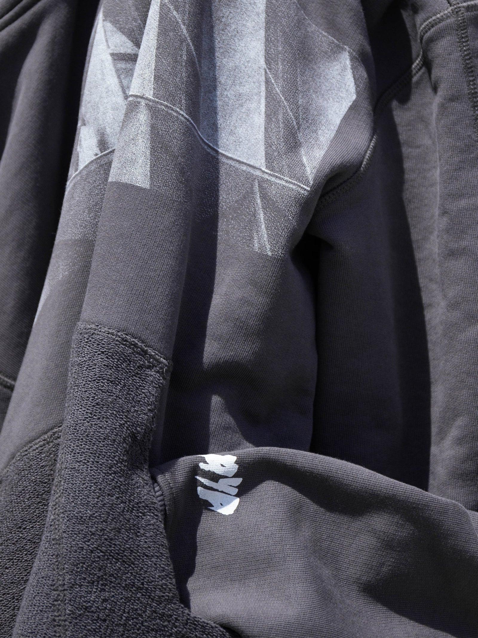 Close-up of a dark gray jacket with brutalist print and brand logo.