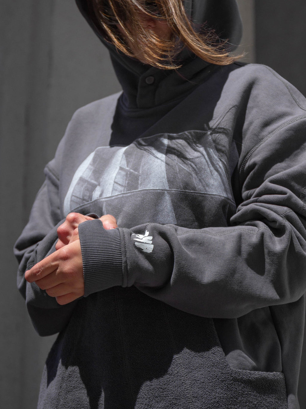 Person wearing a dark gray hoodie with a brand logo on a plain background.